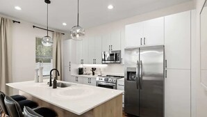 A modern kitchen with white cabinets, stainless steel appliances, a central island with seating, and pendant lighting.