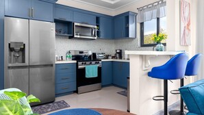 A modern kitchen with blue cabinets, stainless steel appliances, and a small dining area with blue chairs. - The Blooming Blaze W/ Pool (Kingston)