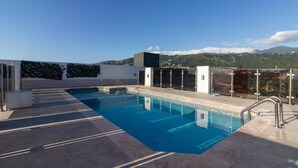 A rooftop swimming pool with clear blue water, a metal ladder, and a view of a mountainous landscape in the background. - The Blooming Blaze W/ Pool (Kingston)