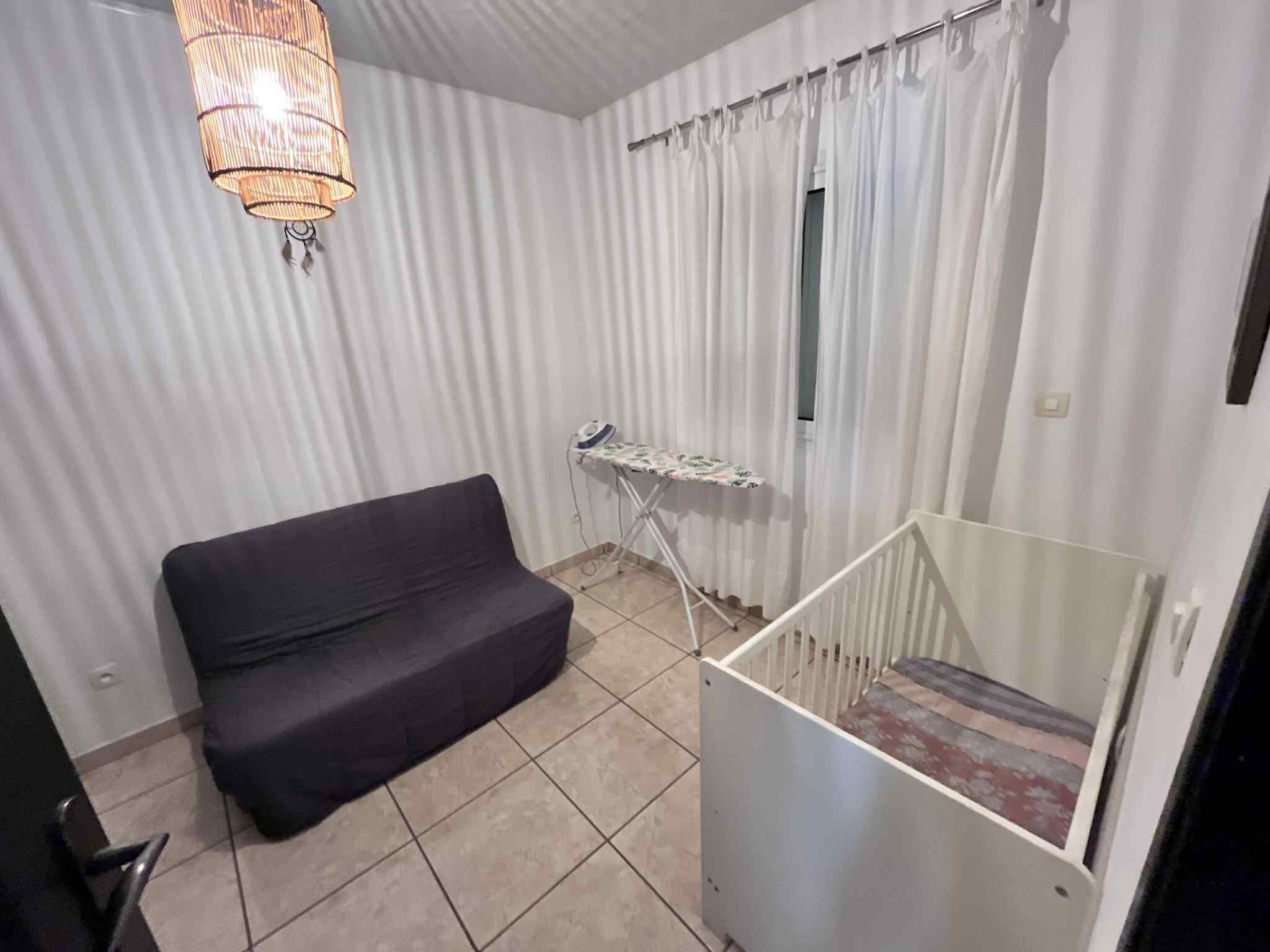 Una habitación pequeña y funcional con un sofá negro, un centro de planchado compacto y una escalera.