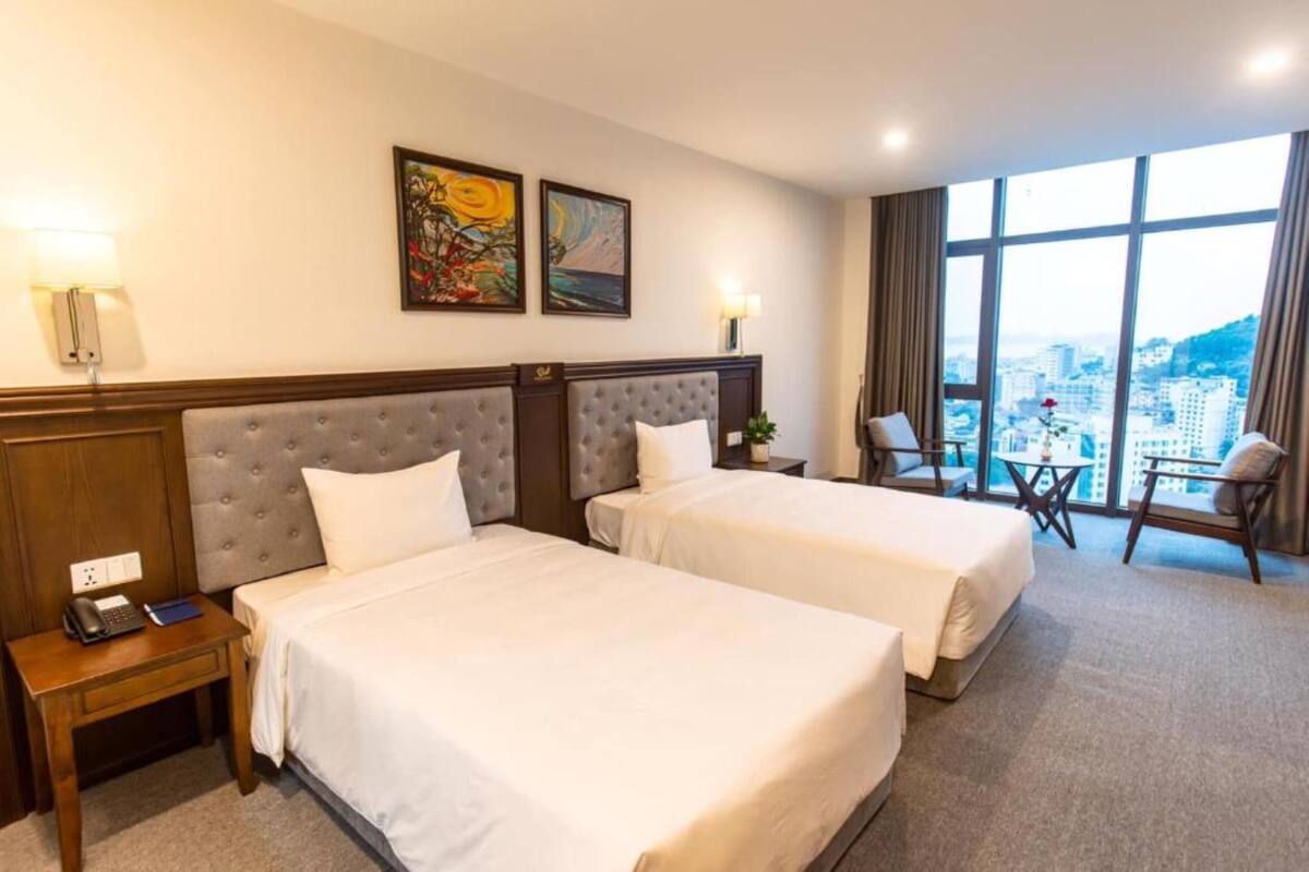 A hotel room with two beds, a desk, a chair, and a view of the city.