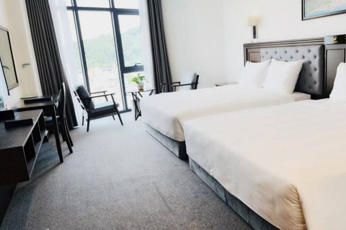 A hotel room with two beds, a desk, a chair, and a large window with curtains.