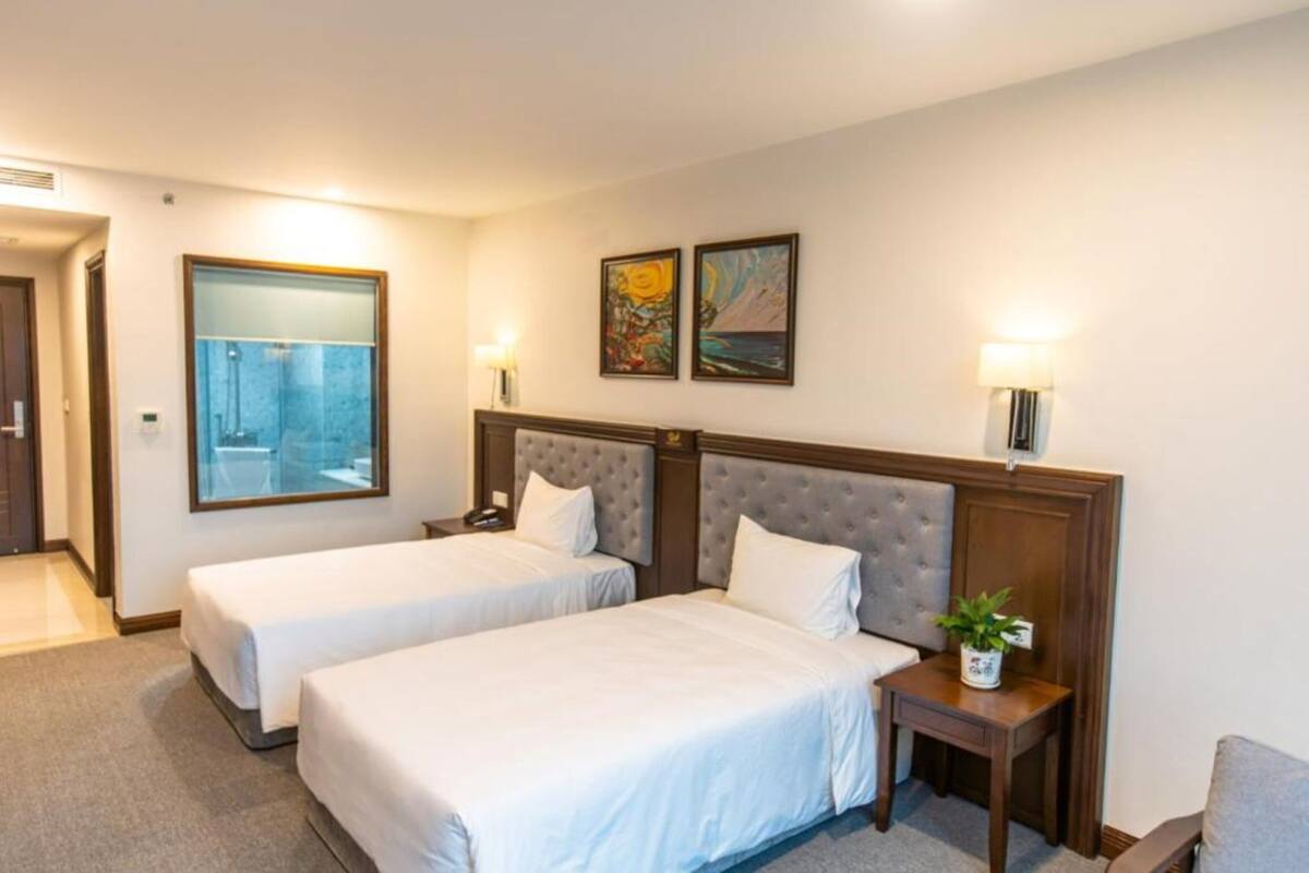 A hotel room with two beds, a small table with a plant, and artwork on the wall.