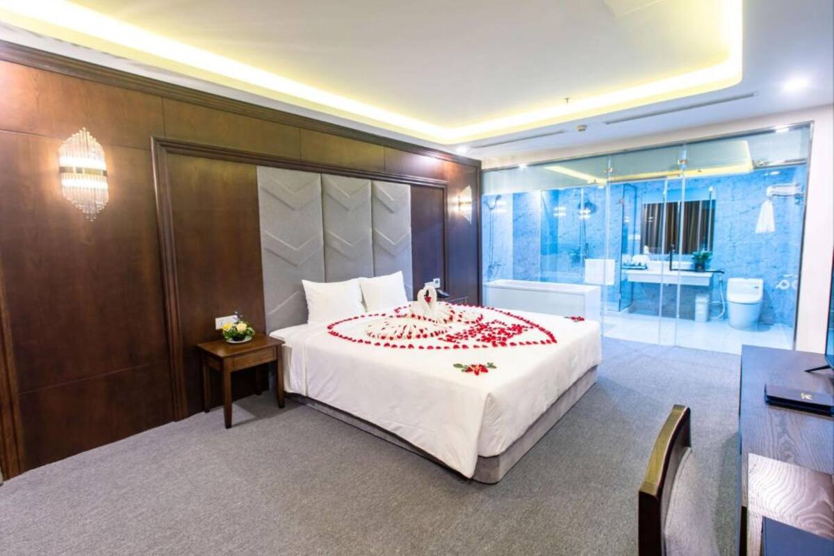 A hotel room with a large bed, a small bedside table, a mirror, and a view of the bathroom.