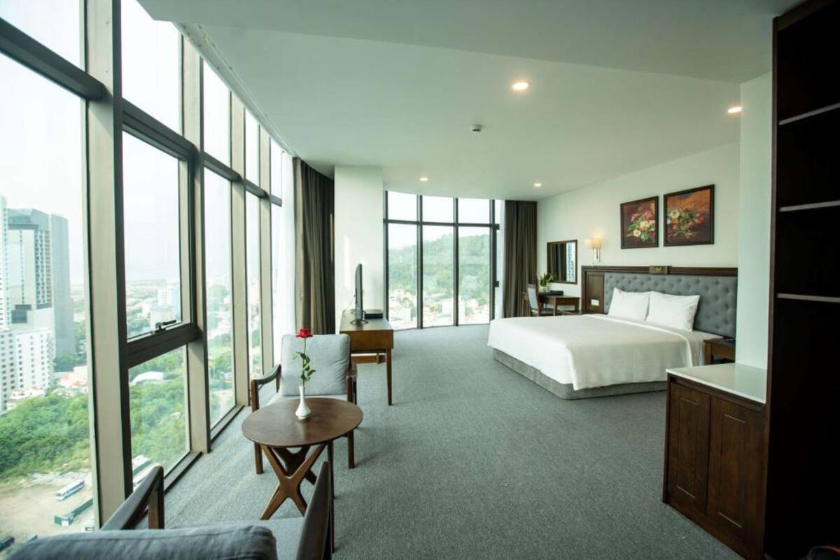 A hotel room with a large bed, a desk, a chair, and a view of the city.
