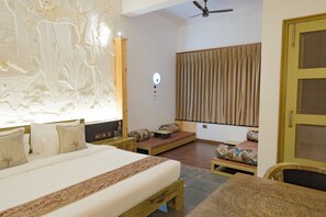 A bedroom with a large bed, a wooden nightstand, a bedside table, a wall-mounted light, a ceiling fan, and a window with curtains.
