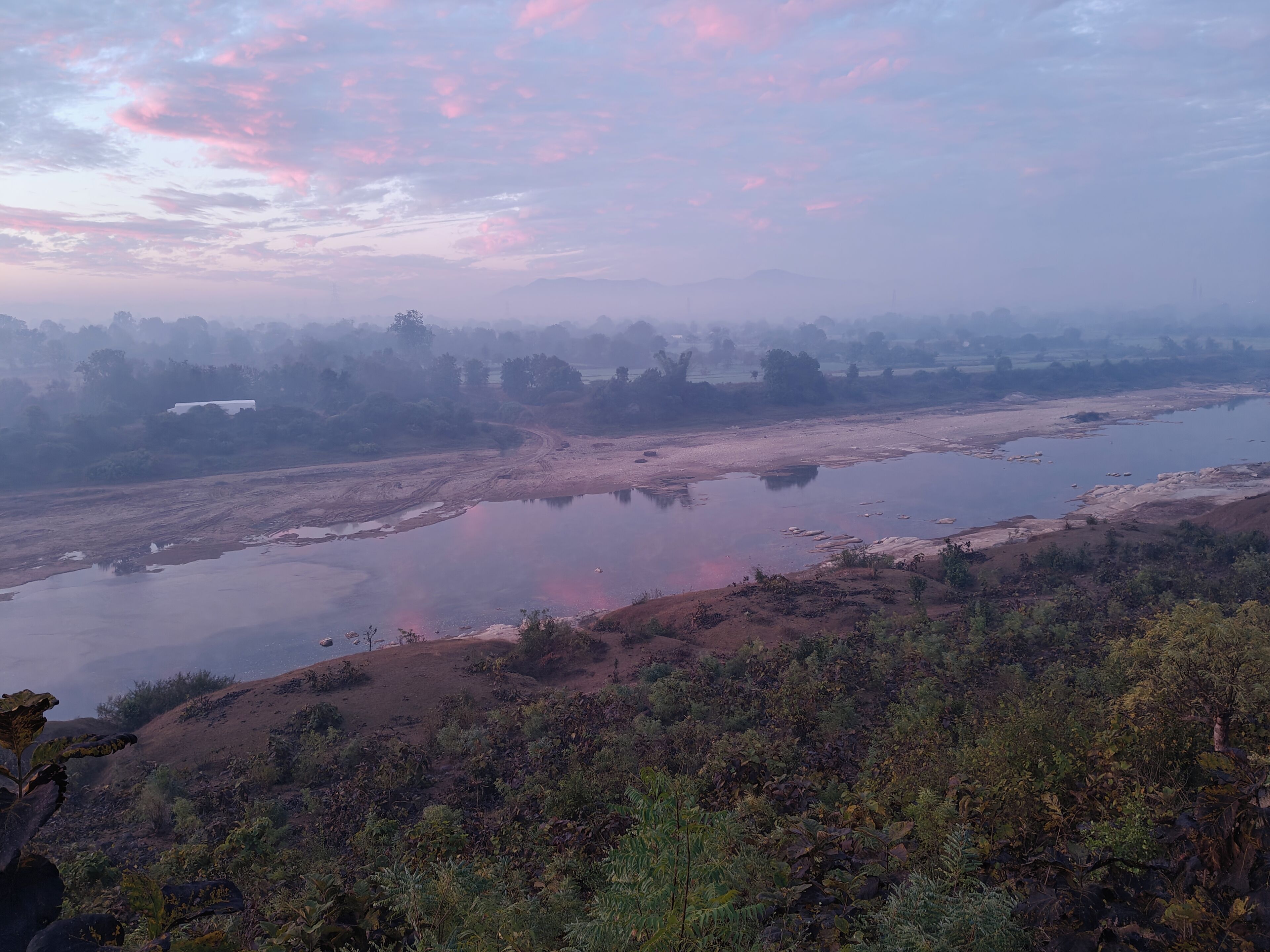 Un río con un puente, rodeado de colinas y árboles.
