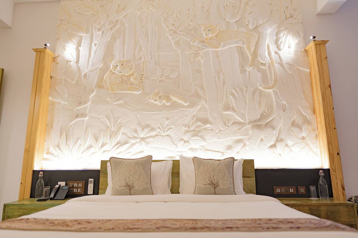 Une chambre avec un grand lit, deux tables de chevet et un mur orné d’un motif de feuilles.