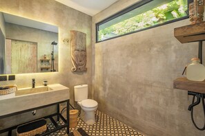A modern bathroom with a large mirror, a sink, a toilet, and a shower area. - Ubud Lila Concept (Ubud)