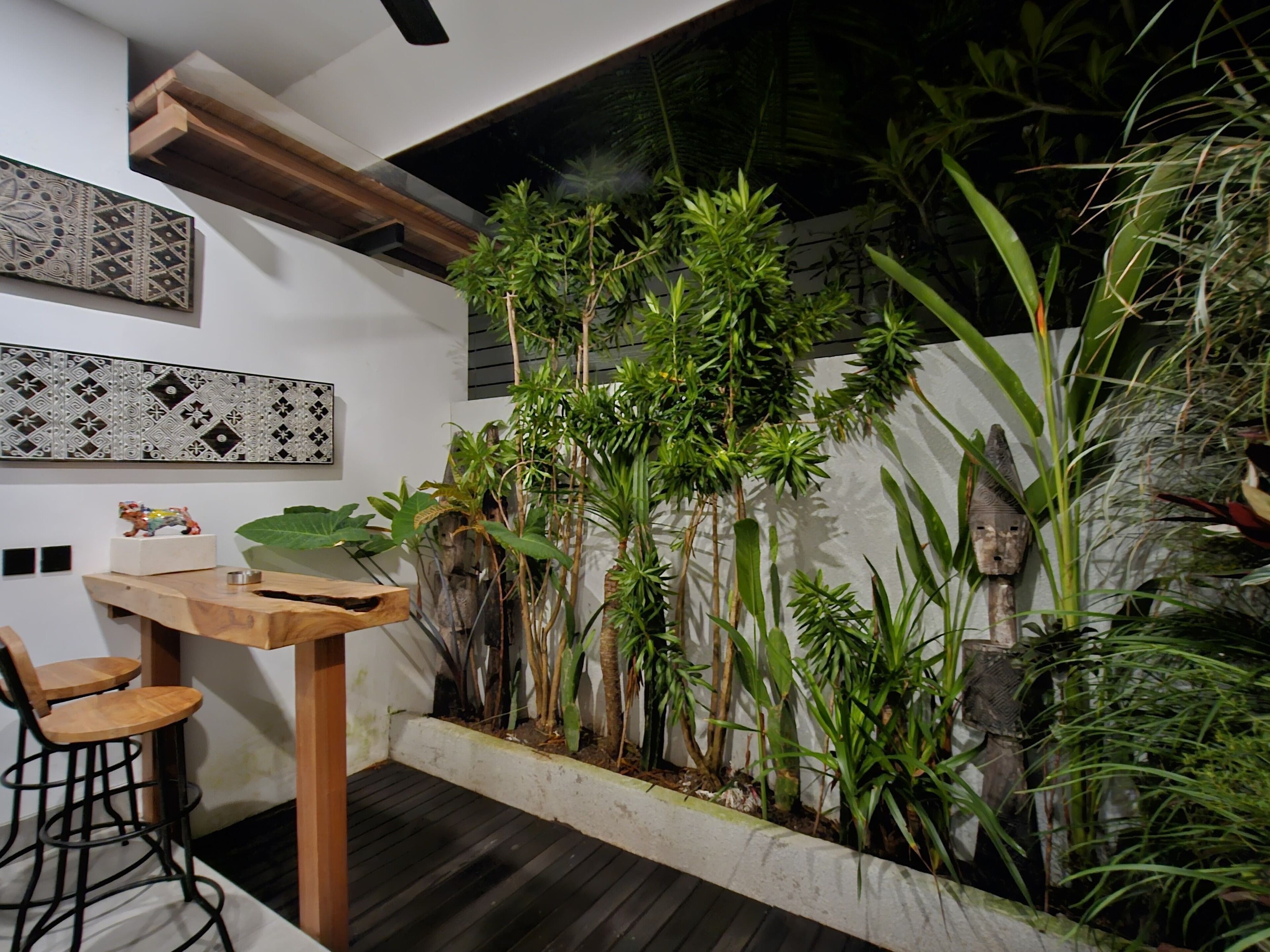 Un interior moderno con una mesa y sillas de madera, una pared decorativa con patrones geométricos y una variedad de plantas verdes.