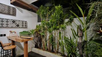 Un interior moderno con una mesa y sillas de madera, una pared decorativa con patrones geométricos y una variedad de plantas verdes.