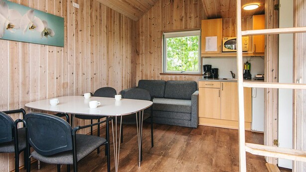 Ein Holzinnenraum mit rundem Tisch, grauem Sofa und einer Küchenzeile mit Holdekor und Fenster.