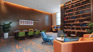 Une salle de conférence moderne, dotée d’une longue table, de chaises vertes et bleues, d’un canapé et d’une bibliothèque agrémentée d’objets décoratifs.