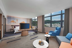 Habitació d'hotel amb un llit, una taula de treball amb un ordinador, una televisió, un sofà i vistes a la ciutat.