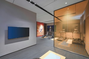 A modern interior with a flat-screen TV mounted on the wall, exercise equipment, and a glass partition. - Hampton BY Hilton Shenzhen Yuanshan (Shenzhen)