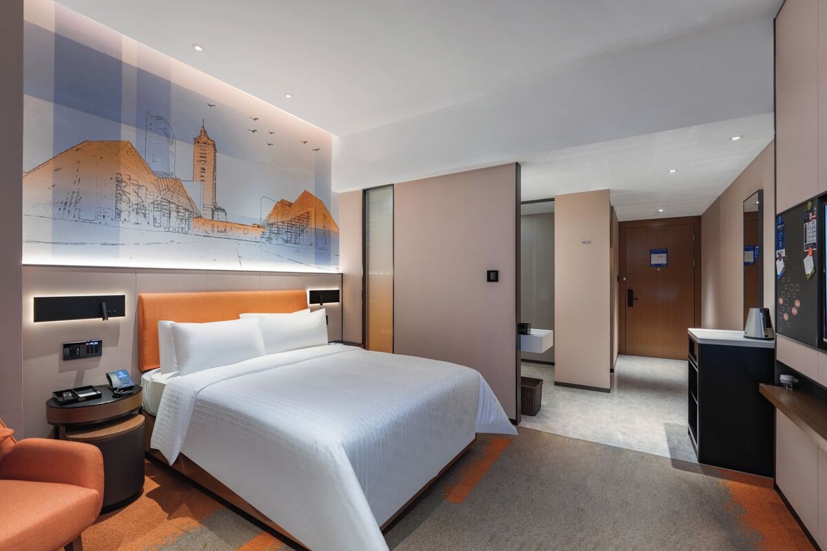 A hotel room with a large bed, a desk with a computer, a chair, a TV, and a painting on the wall.