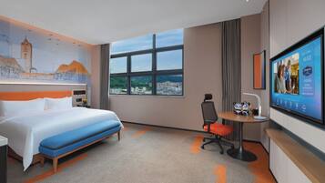 Habitación de hotel con una cama grande, un escritorio, una silla, un televisor y vistas a la ciudad.