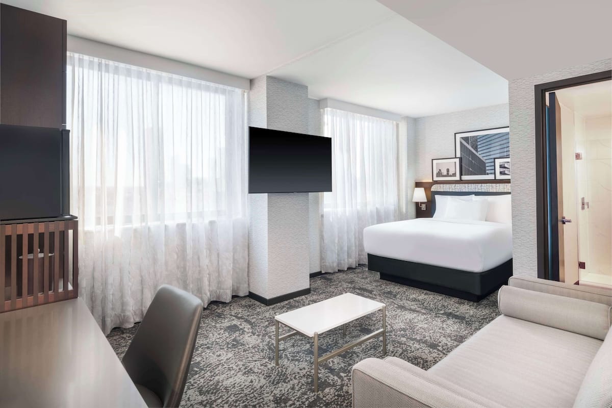 Une chambre d’hôtel avec un lit, un téléviseur fixé au mur, une petite table et un canapé.