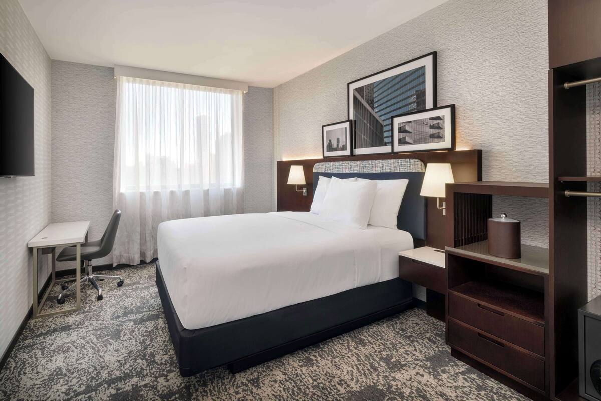 Une chambre d’hôtel avec un grand lit, un bureau, une chaise, une télévision et une fenêtre avec des rideaux.