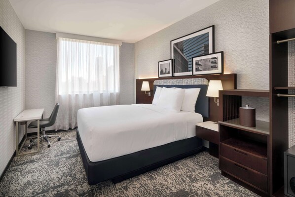 A hotel room with a large bed, a desk, a chair, a TV, and a window with curtains. - DoubleTree by Hilton Long Island City, NY (Long Island City)