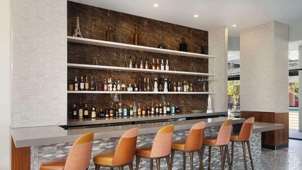 Een moderne bar met een marmeren achterwand, meerdere flessenplanken en een lange bar.