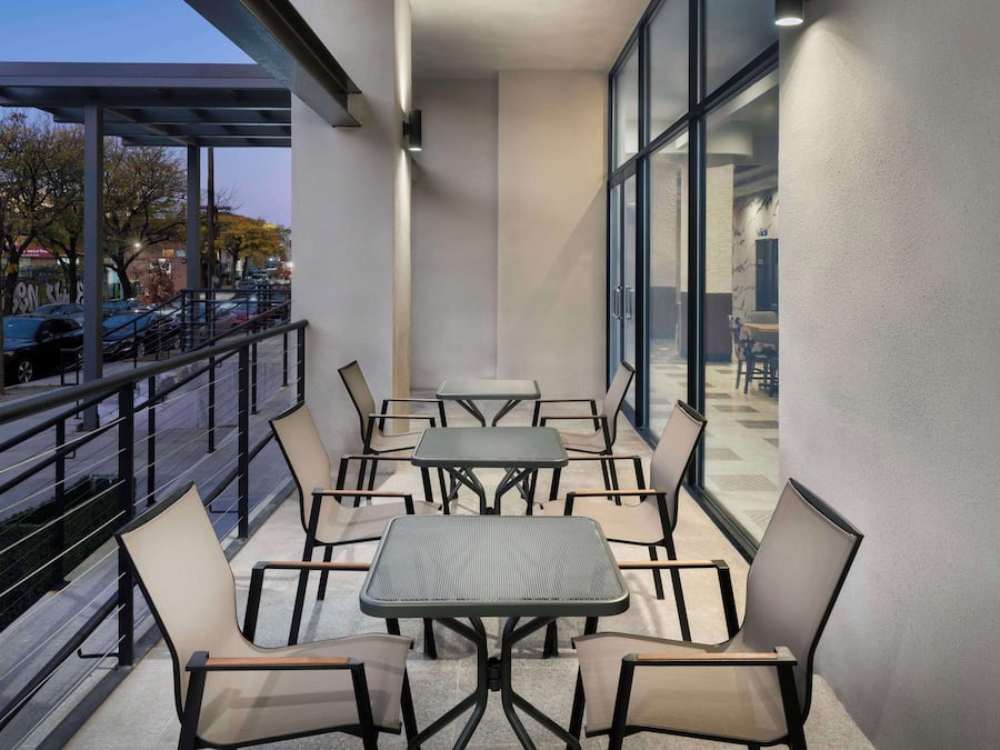 Un balcón con mobiliario exterior, ventanas amplias y vista a coches estacionados.