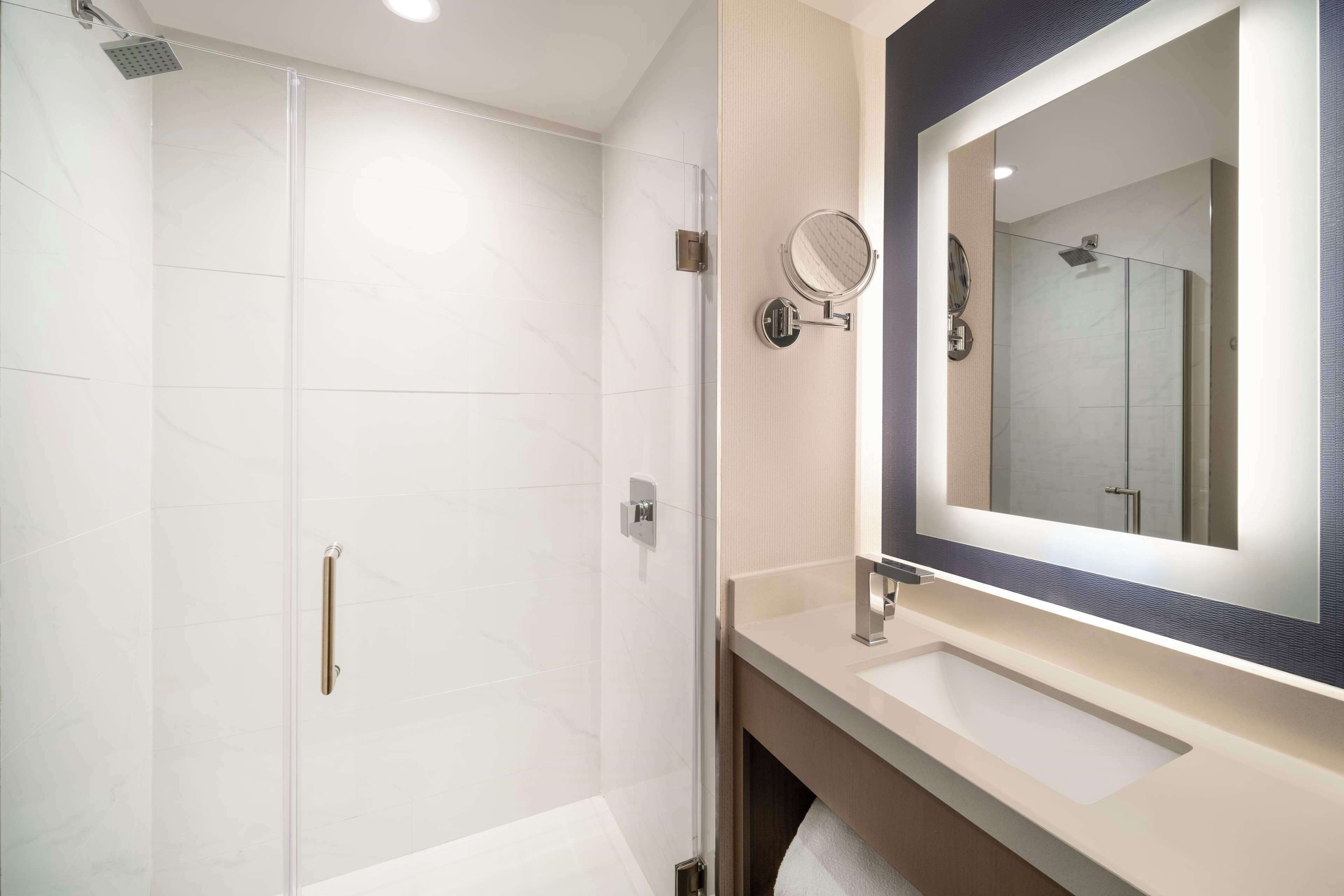 Un baño moderno con cabina de ducha de vidrio, un espejo grande y un mueble de tocador con lavabo.