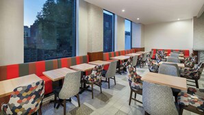 Een restaurant met hoge tafels en zitjes, stoelen met een patroon en grote ramen met uitzicht op buiten.