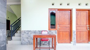 A wooden table with a red chair in front of a set of double doors. - Hotel O Sleman Near Bandara Adi Sutjipto Formerly Joglo Sorogenen (Ngemplak)