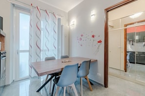 A modern dining area with a wooden table, blue chairs, a glass partition, and a kitchen visible through the glass.