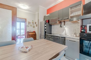 A modern kitchen with stainless steel appliances, a dining area with a wooden table, and a view of the living room.