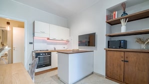 A modern kitchen with white cabinetry, a central island, a built-in microwave, and a wooden cabinet with books and decorative items. - GuestHost - Comfortable apartment, able to accommodate up to 4 people. The accommodation is located in a refined period building in the center of Turin, a few meters from Piazza Castello and the Royal Palace, a short distance from every essential service (Torino)