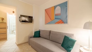 A living room with a sofa, a TV mounted on the wall, and a painting above the sofa. - GuestHost - Comfortable apartment, able to accommodate up to 4 people. The accommodation is located in a refined period building in the center of Turin, a few meters from Piazza Castello and the Royal Palace, a short distance from every essential service (Torino)
