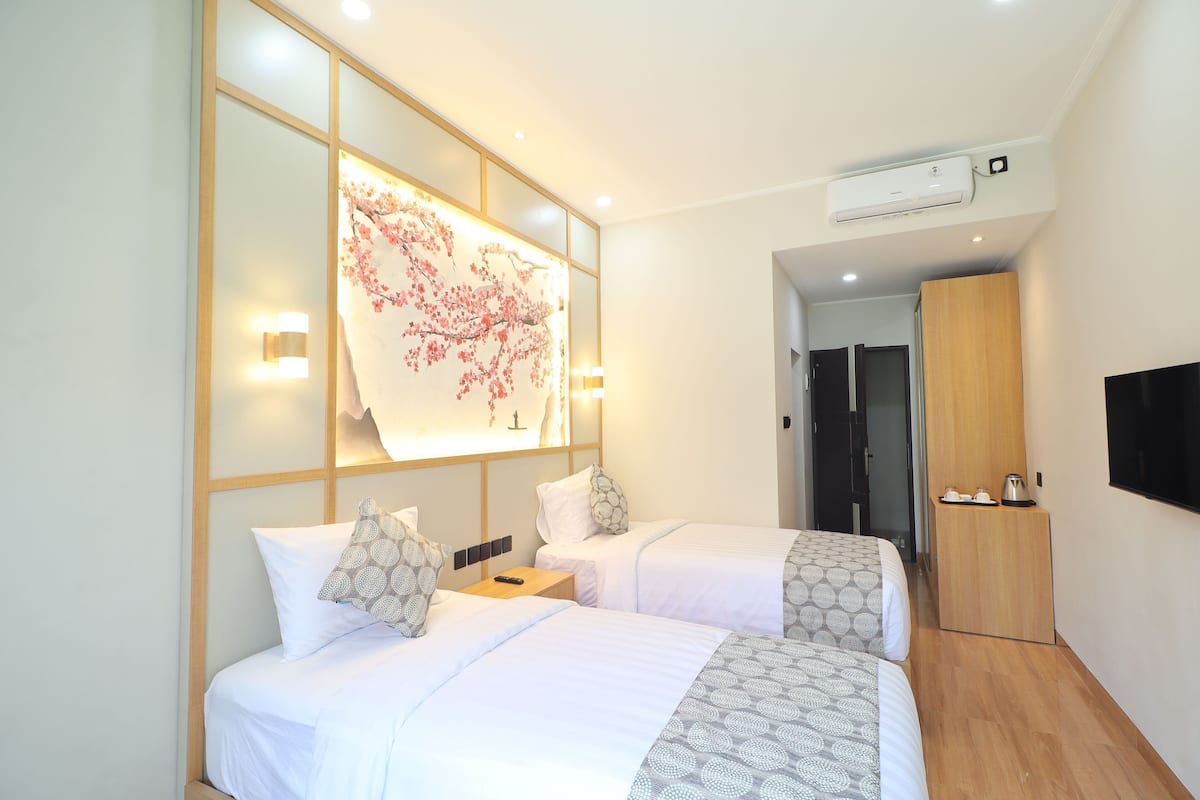 A hotel room with two beds, a wall-mounted air conditioner, a TV, and a wooden wardrobe.