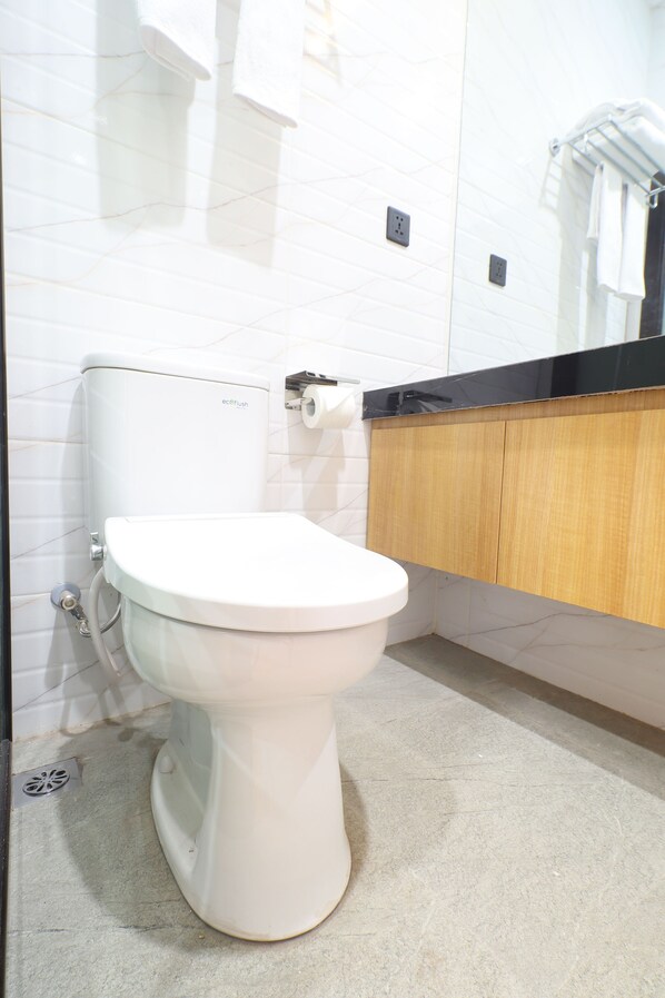 A modern bathroom with a white toilet, a wooden vanity, and a tiled wall.