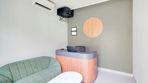 A reception desk with a laptop, a green sofa, and a round wooden accent wall. - Collection O Samurai Hotel (Denpasar)