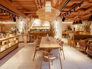 A spacious, modern dining area with a long wooden table and chairs, surrounded by shelves and potted plants. - Wren Urban Nest (Dublin)