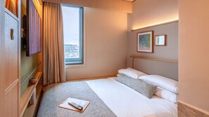 A hotel room with a bed, a window with curtains, a mounted TV, and framed pictures on the wall. - Wren Urban Nest (Dublin)
