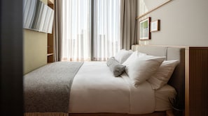 A neatly made bed with white linens and a gray throw blanket, a wooden headboard, and a window with sheer curtains allowing natural light. - Wren Urban Nest (Dublin)