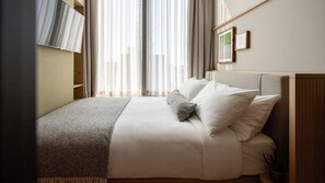 A neatly made bed with white linens and a gray throw blanket, a wooden headboard, and sheer curtains allowing natural light. - Wren Urban Nest (Dublin)