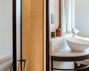 A bathroom with a large mirror, a white sink, and a shower area. - Wren Urban Nest (Dublin)