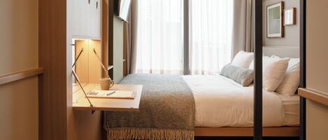 Une chambre à coucher avec un lit, une table de chevet, une lampe et une fenêtre avec des rideaux.