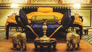 A bed with a decorative headboard, two nightstands with lamps, and a small table with an elephant-shaped object. - The Umaid Vilas Royal Heritage Haveli (Jaipur)