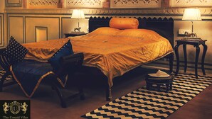 A traditional room with a bed, two side tables, a chair, and a patterned rug. - The Umaid Vilas Royal Heritage Haveli (Jaipur)