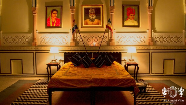 A hotel room with a bed, two lamps, a patterned rug, and three framed portraits on the wall. - The Umaid Vilas Royal Heritage Haveli (Jaipur)