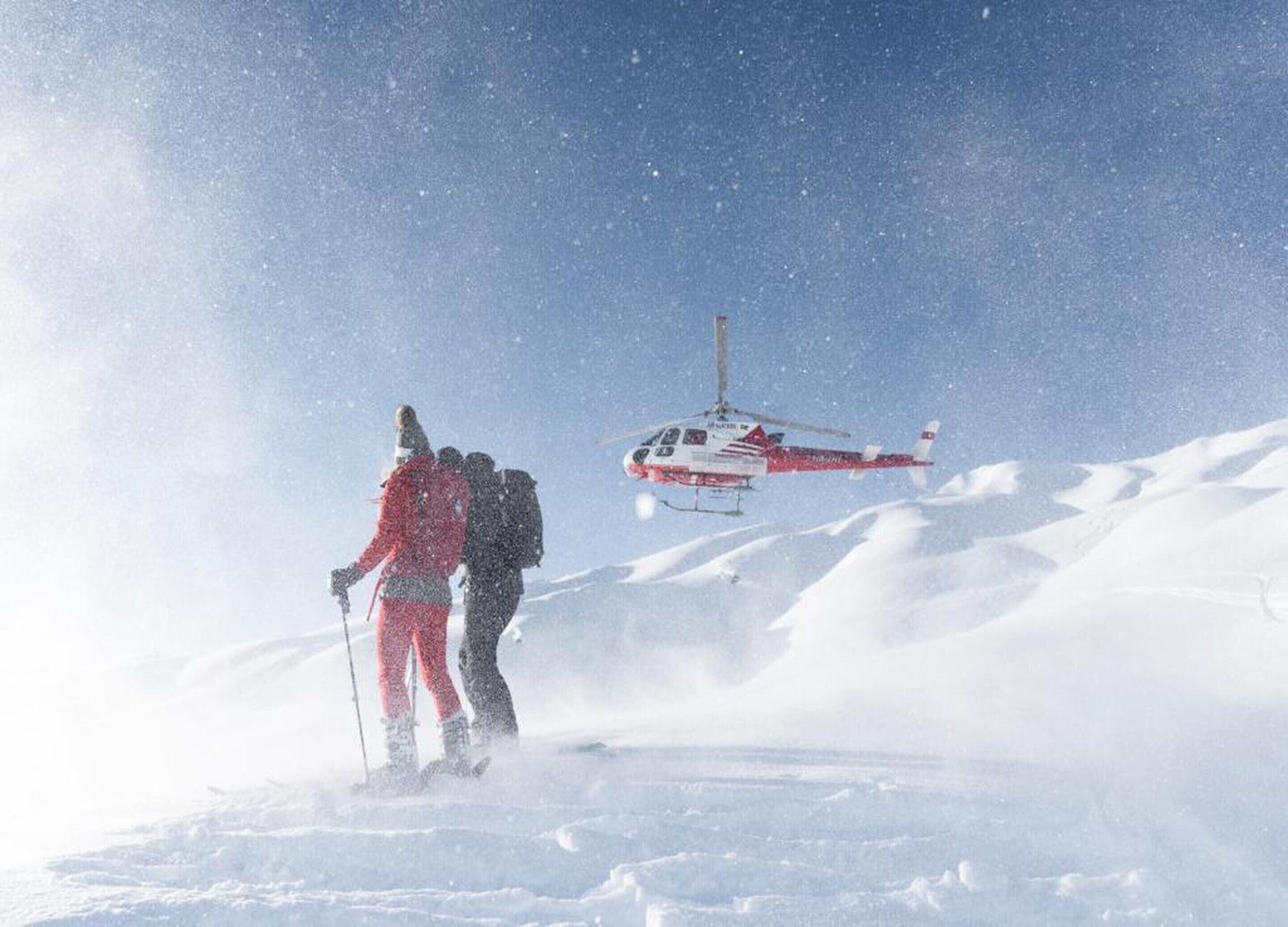 A helicopter flying over a snowy landscape with two people skiing below.