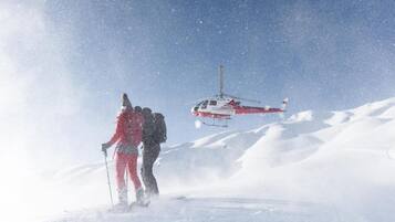 A helicopter flying over a snowy landscape with two people skiing below.