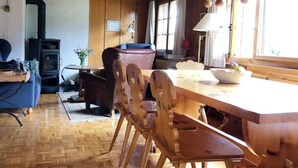 Um quarto acolhedor com teto de madeira, uma mesa de jantar com cadeiras, um sofá, uma lareira e uma janela com cortinas.