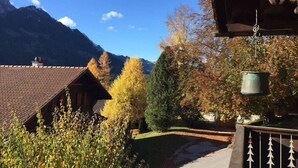 Uma cabana na montanha com telhado de telhas, rodeada por folhagem de outono e um céu azul límpido.