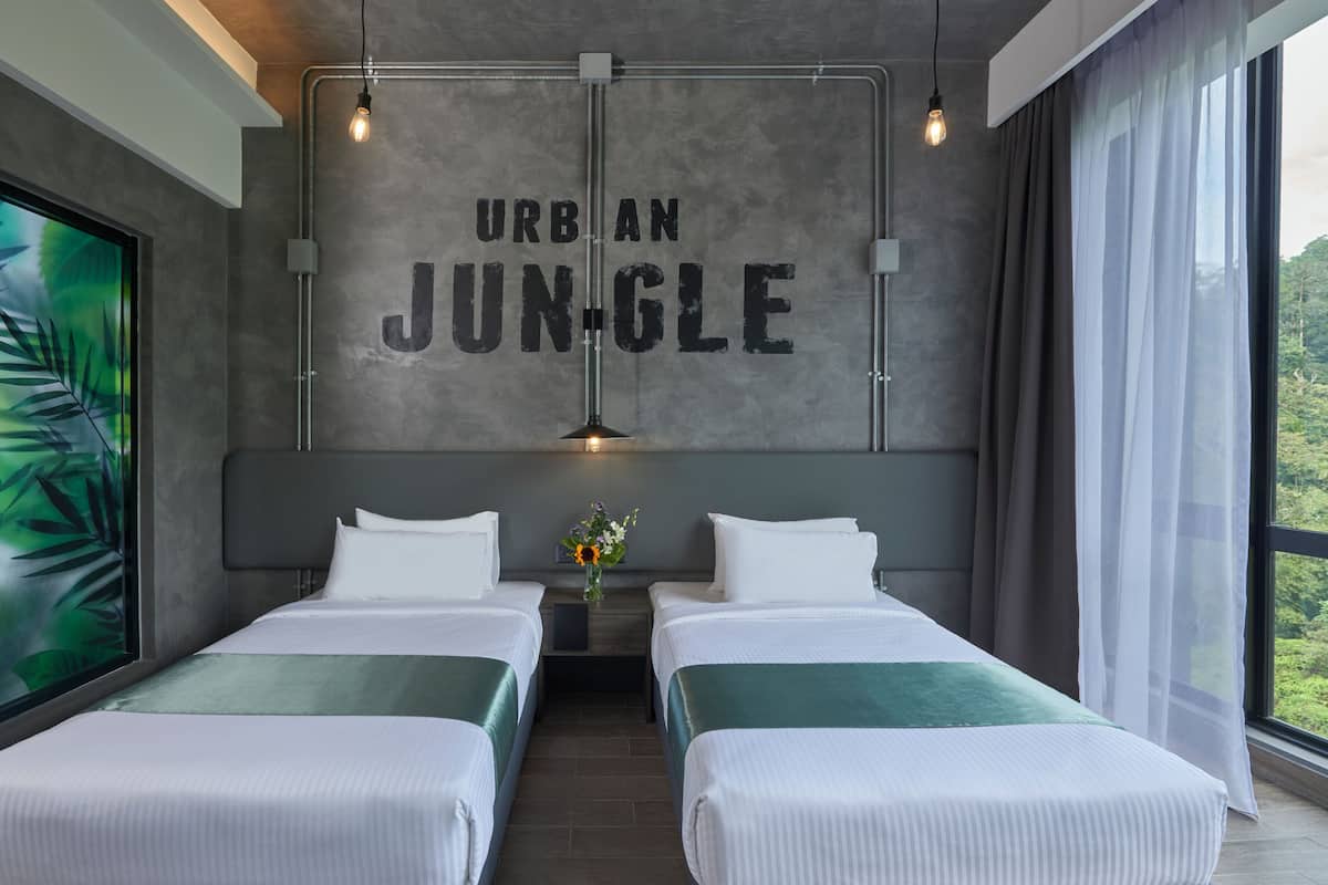 A modern hotel room with two beds, a large window with a view, and a wall with the text "URBAN JUNGLE".